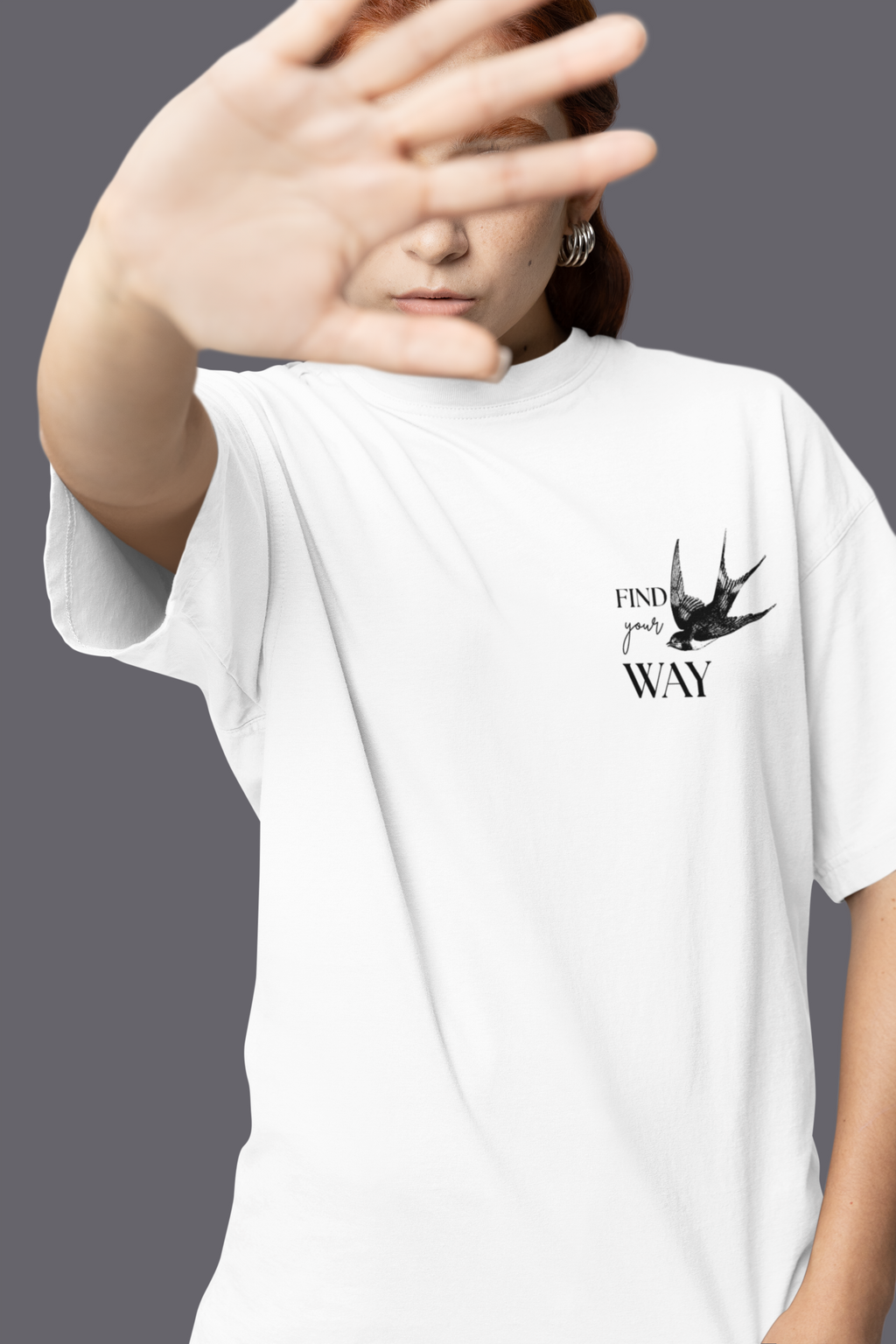 Woman in oversized white t-shirt with bird graphic and 'Find your way' text, studio backdrop