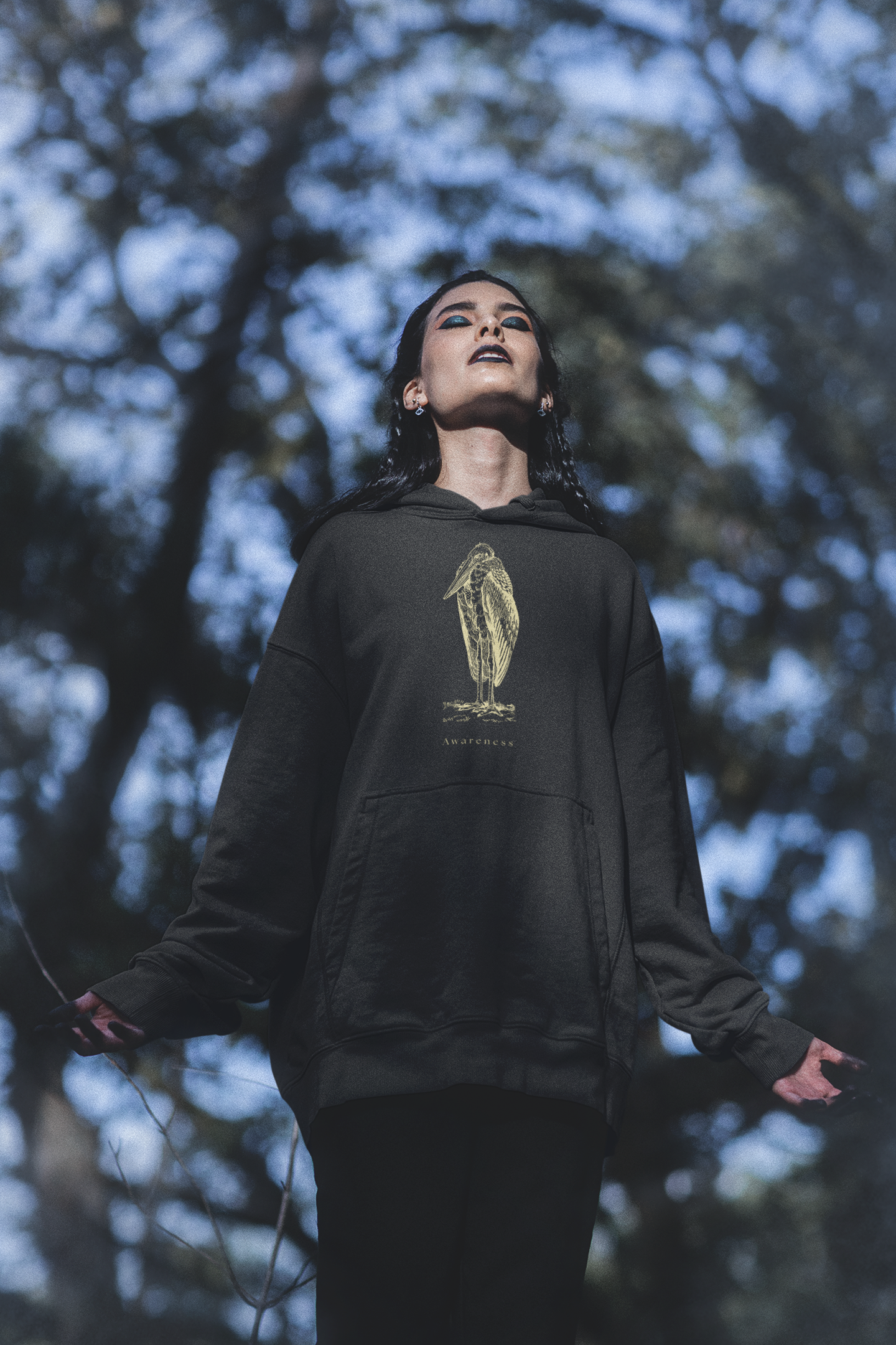 Woman wearing oversized pullover hoodie with bird design, standing in a forest
